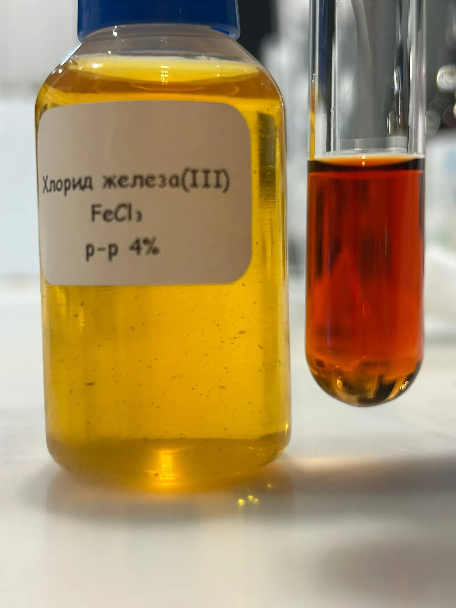 Флакон с раствором хлорида железа(III) из набора и рядом пробирка с тёмно-красным роданидом железа